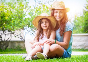 Happy family in the garden, beautiful mother with her little cute daughter sitting on fresh green grass on a backyard, with pleasure spending time together