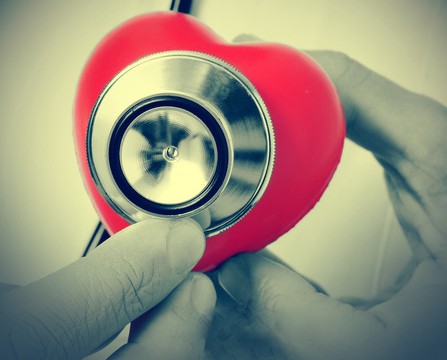 closeup of a doctor auscultating a red heart with a stethoscope and the text world heart day